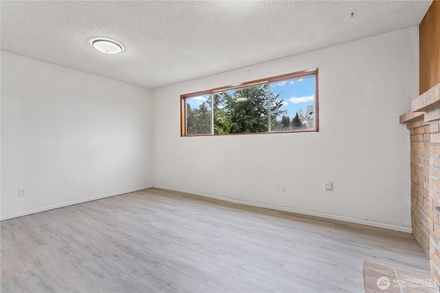 spare room with light wood finished floors, a brick fireplace, a textured ceiling, and baseboards