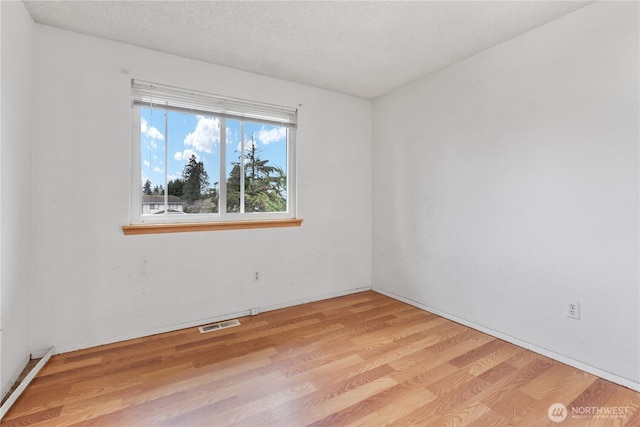 unfurnished room featuring visible vents, light wood finished floors, and a textured ceiling