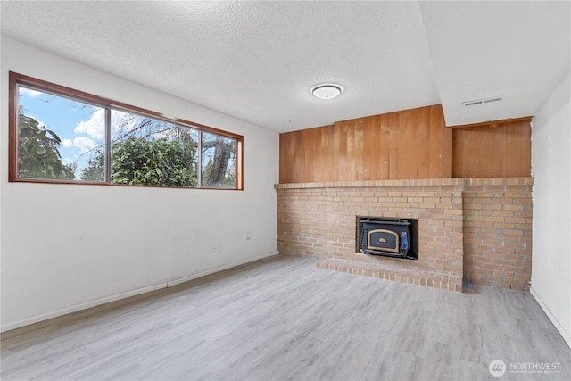 unfurnished living room featuring visible vents, a textured ceiling, wood finished floors, baseboards, and a wood stove