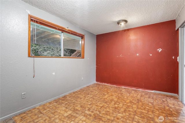 spare room with a textured ceiling and baseboards