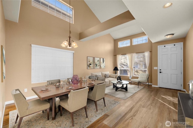 dining area featuring a notable chandelier, a high ceiling, baseboards, and wood finished floors