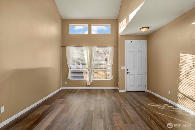 entryway featuring a towering ceiling, baseboards, and dark wood finished floors