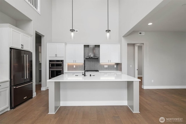 kitchen featuring wall chimney range hood, dobule oven black, high quality fridge, and a high ceiling