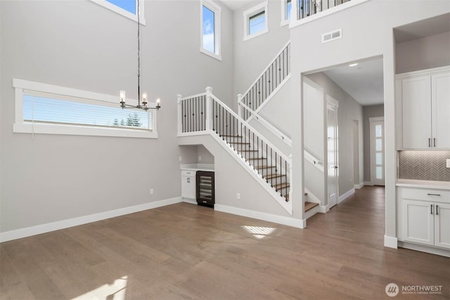 unfurnished living room with a high ceiling, stairs, baseboards, wood finished floors, and wine cooler