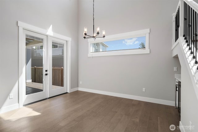 unfurnished dining area with an inviting chandelier, baseboards, french doors, and dark wood-style flooring