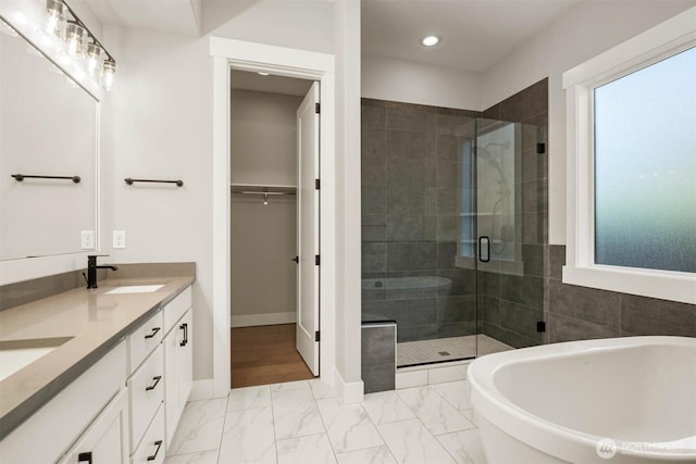 bathroom with double vanity, marble finish floor, a freestanding bath, a shower stall, and a sink