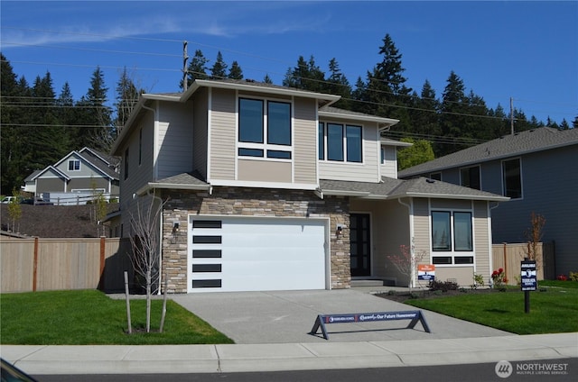 prairie-style home with driveway, fence, a front lawn, an attached garage, and stone siding
