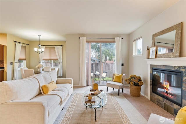 living room featuring a tiled fireplace, a notable chandelier, baseboards, and light carpet