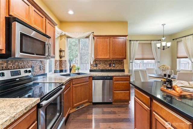 kitchen with brown cabinets, a sink, dark wood finished floors, stainless steel appliances, and hanging light fixtures