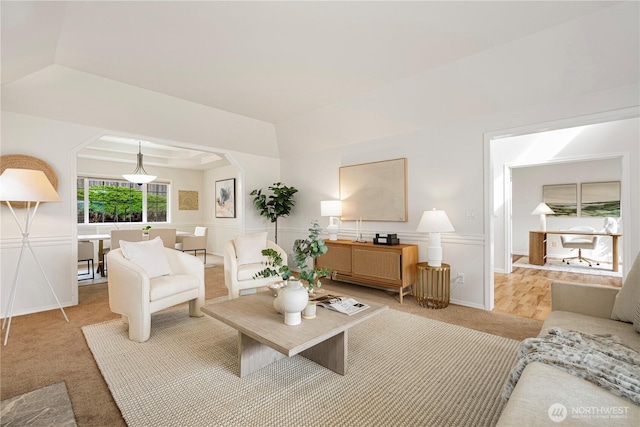 living area with a tray ceiling, arched walkways, wainscoting, light carpet, and a decorative wall