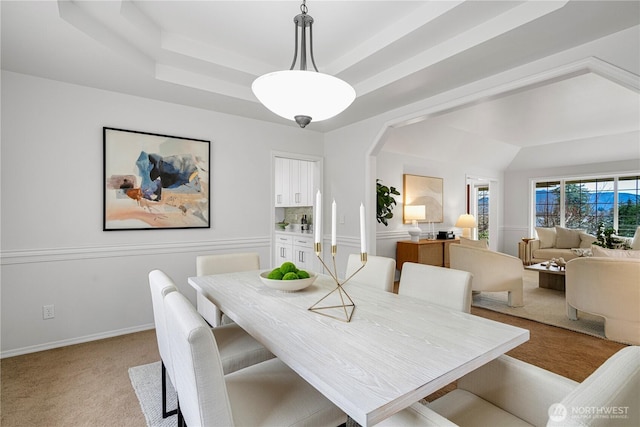 dining space with a tray ceiling, light carpet, arched walkways, and baseboards