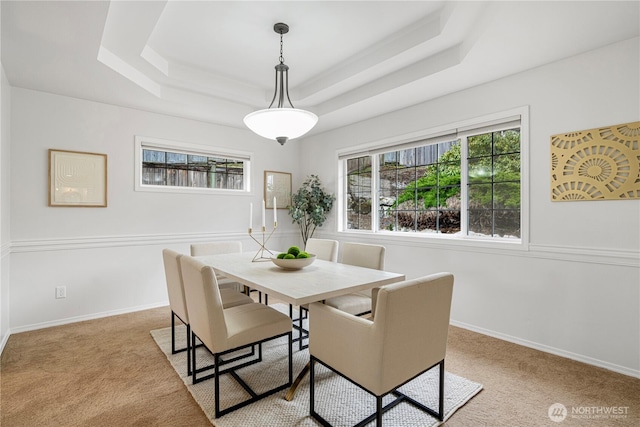 carpeted dining space with a tray ceiling and baseboards