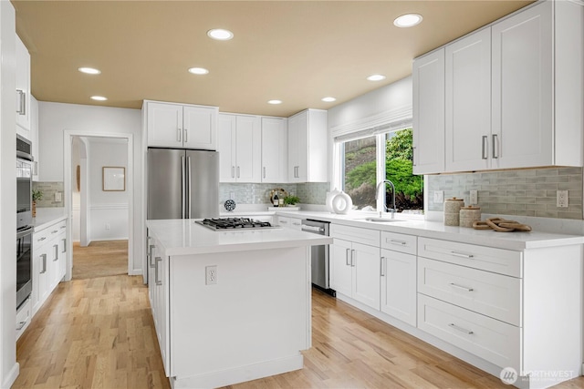 kitchen featuring a kitchen island, a sink, light countertops, light wood-style floors, and appliances with stainless steel finishes