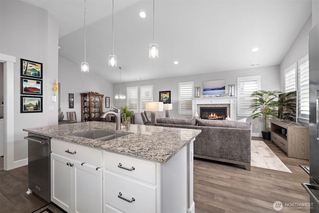 kitchen with dishwasher, an island with sink, wood finished floors, vaulted ceiling, and a sink