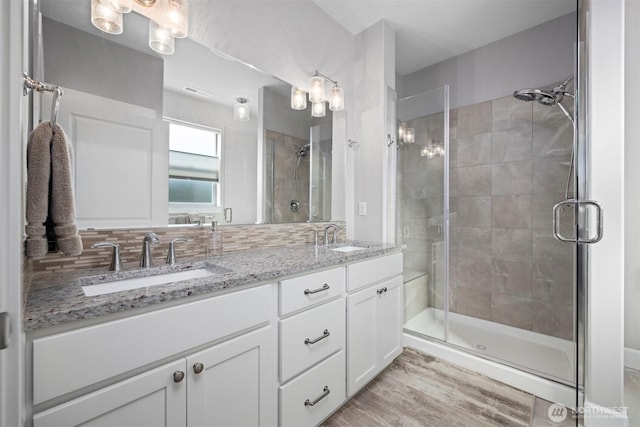 full bath featuring a stall shower, wood finished floors, a sink, and double vanity