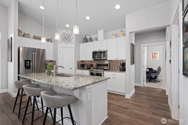 kitchen with white cabinets, appliances with stainless steel finishes, a sink, a kitchen bar, and backsplash