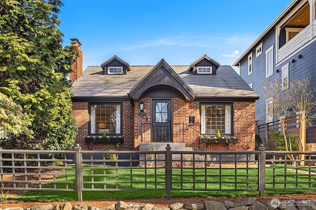 view of front facade with a fenced front yard, a front yard, brick siding, and a chimney