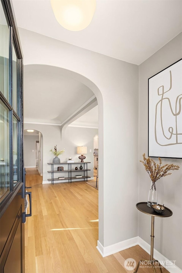 corridor with arched walkways, light wood-style flooring, and baseboards