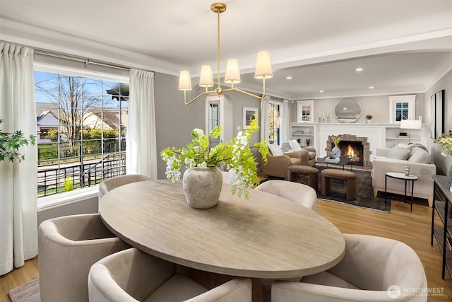 dining room with a notable chandelier, light wood finished floors, recessed lighting, ornamental molding, and a lit fireplace