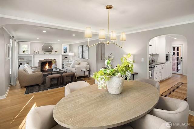 dining room with recessed lighting, light wood-style flooring, crown molding, and a lit fireplace