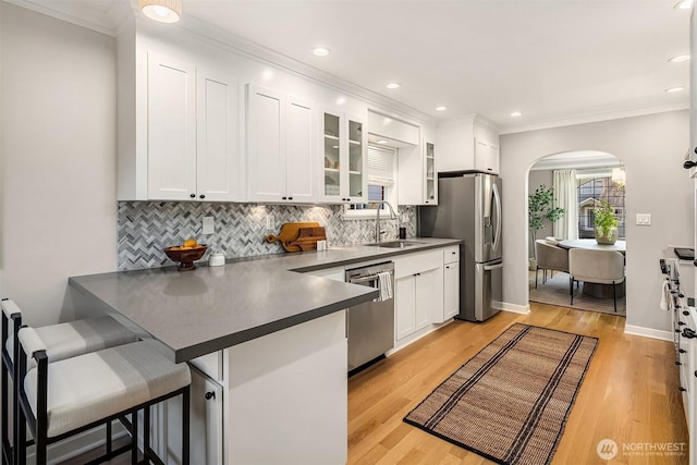 kitchen with arched walkways, a breakfast bar, a peninsula, stainless steel appliances, and a sink