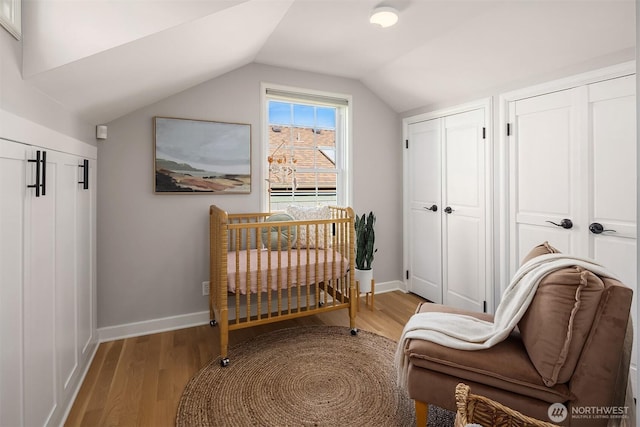 bedroom with light wood-style floors, baseboards, vaulted ceiling, and two closets