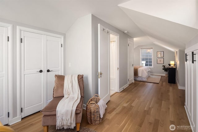 hallway with light wood-type flooring, baseboards, and vaulted ceiling