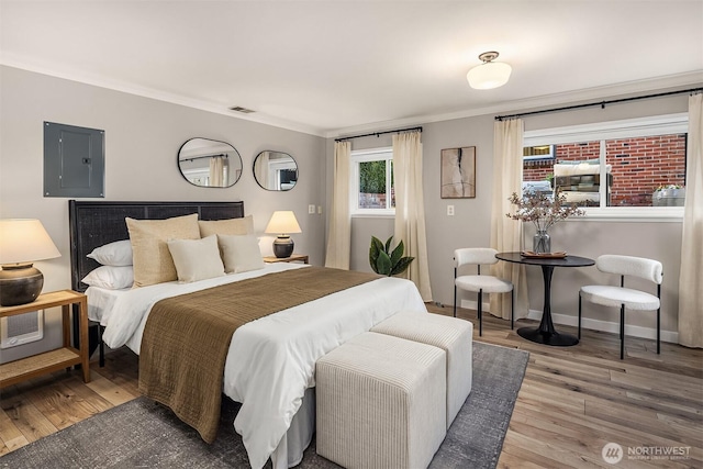 bedroom with wood finished floors, visible vents, baseboards, ornamental molding, and electric panel