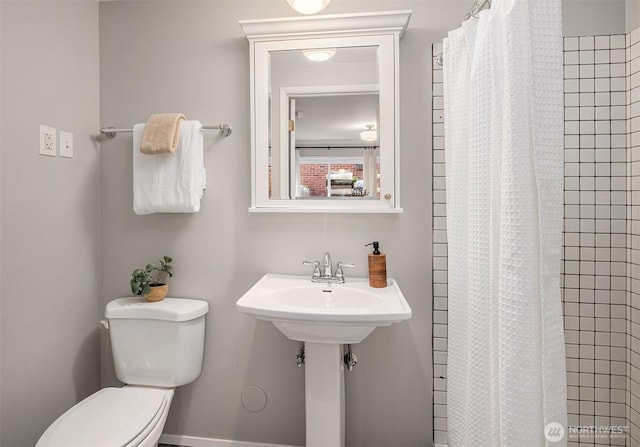 bathroom featuring toilet, baseboards, and tiled shower