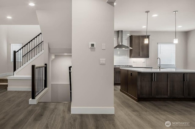 kitchen featuring dark brown cabinetry, decorative backsplash, dark wood finished floors, wall chimney range hood, and a sink