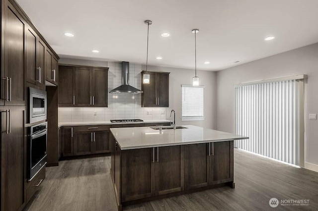 kitchen with dark wood-style flooring, stainless steel appliances, a sink, wall chimney range hood, and dark brown cabinets