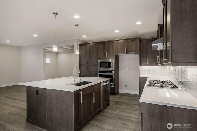 kitchen featuring dark wood-style flooring, a sink, wall chimney range hood, appliances with stainless steel finishes, and decorative backsplash