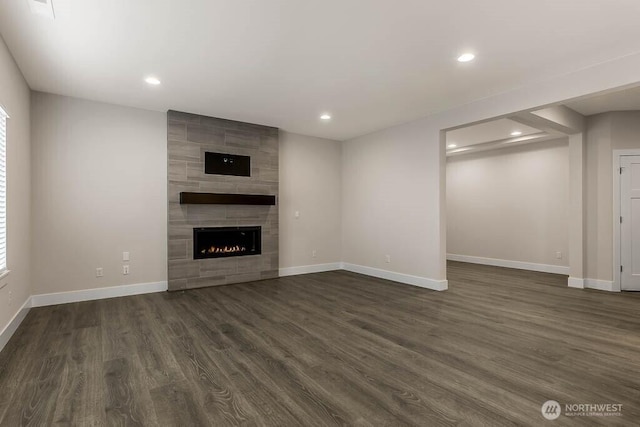 unfurnished living room with dark wood-style floors, a tile fireplace, baseboards, and recessed lighting