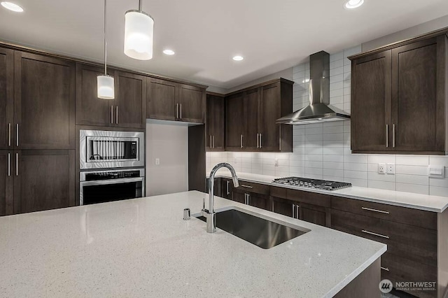 kitchen with stainless steel appliances, a sink, wall chimney range hood, decorative backsplash, and pendant lighting