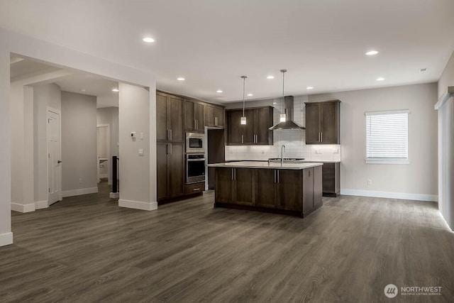 kitchen with dark brown cabinetry, stainless steel appliances, dark wood-type flooring, wall chimney exhaust hood, and tasteful backsplash