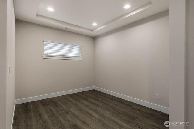 empty room with a tray ceiling, dark wood-style flooring, recessed lighting, and baseboards