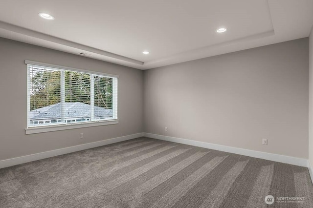 carpeted spare room featuring recessed lighting, a raised ceiling, and baseboards