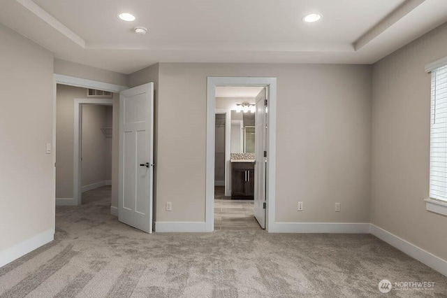 unfurnished bedroom with recessed lighting, a raised ceiling, light colored carpet, visible vents, and baseboards