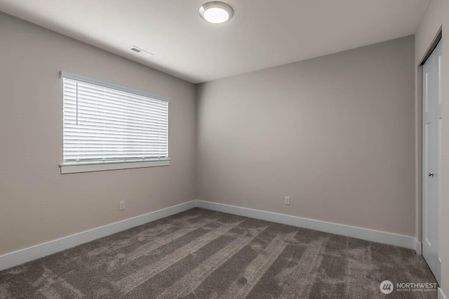 unfurnished room with dark colored carpet, visible vents, and baseboards