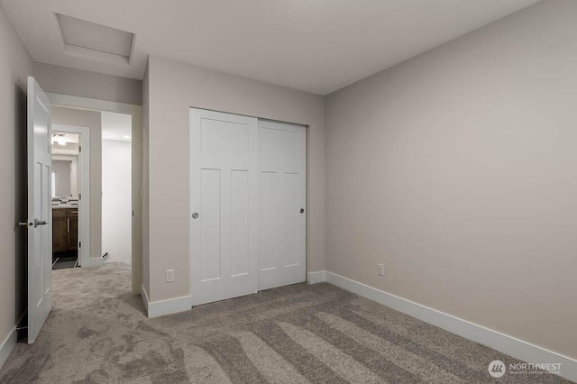 unfurnished bedroom with attic access, a closet, baseboards, and carpet flooring