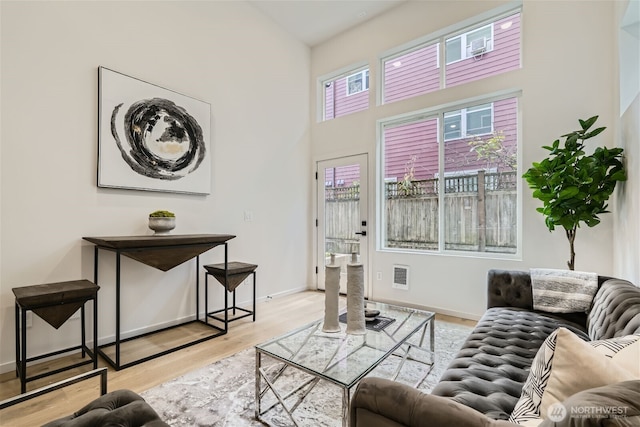 living room with light wood finished floors, a towering ceiling, visible vents, and baseboards