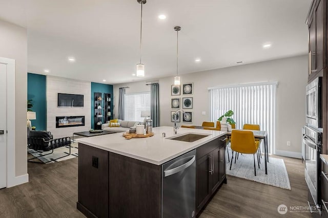 kitchen featuring stainless steel appliances, a sink, dark brown cabinets, light countertops, and a tiled fireplace