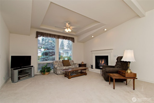 living room featuring ceiling fan, carpet, a raised ceiling, and a glass covered fireplace