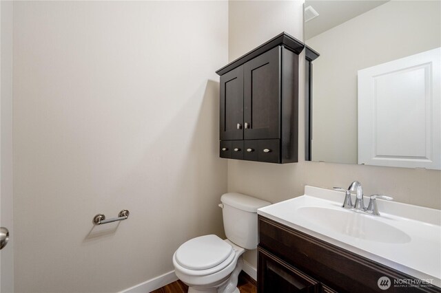 half bath featuring baseboards, toilet, and vanity