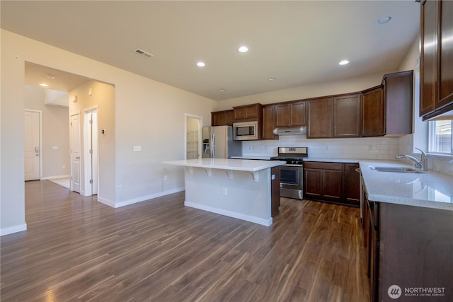 kitchen featuring a sink, under cabinet range hood, decorative backsplash, stainless steel appliances, and dark wood-style flooring