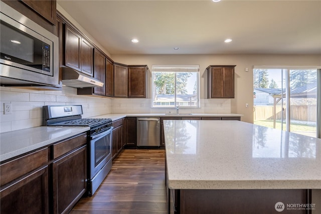 kitchen featuring under cabinet range hood, light stone counters, a sink, a kitchen island, and appliances with stainless steel finishes