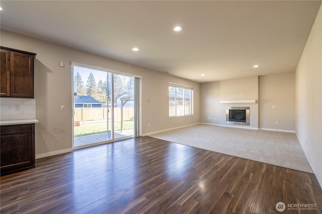 unfurnished living room with a glass covered fireplace, recessed lighting, wood finished floors, and baseboards