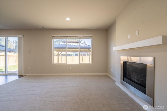 unfurnished living room featuring a glass covered fireplace, visible vents, baseboards, and carpet