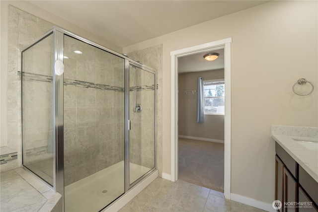 full bathroom featuring a stall shower, vanity, a walk in closet, and baseboards