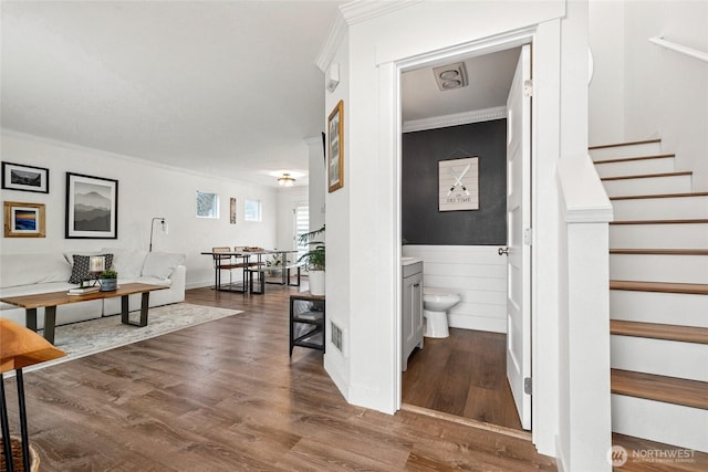 hall featuring visible vents, wainscoting, wood finished floors, stairs, and crown molding